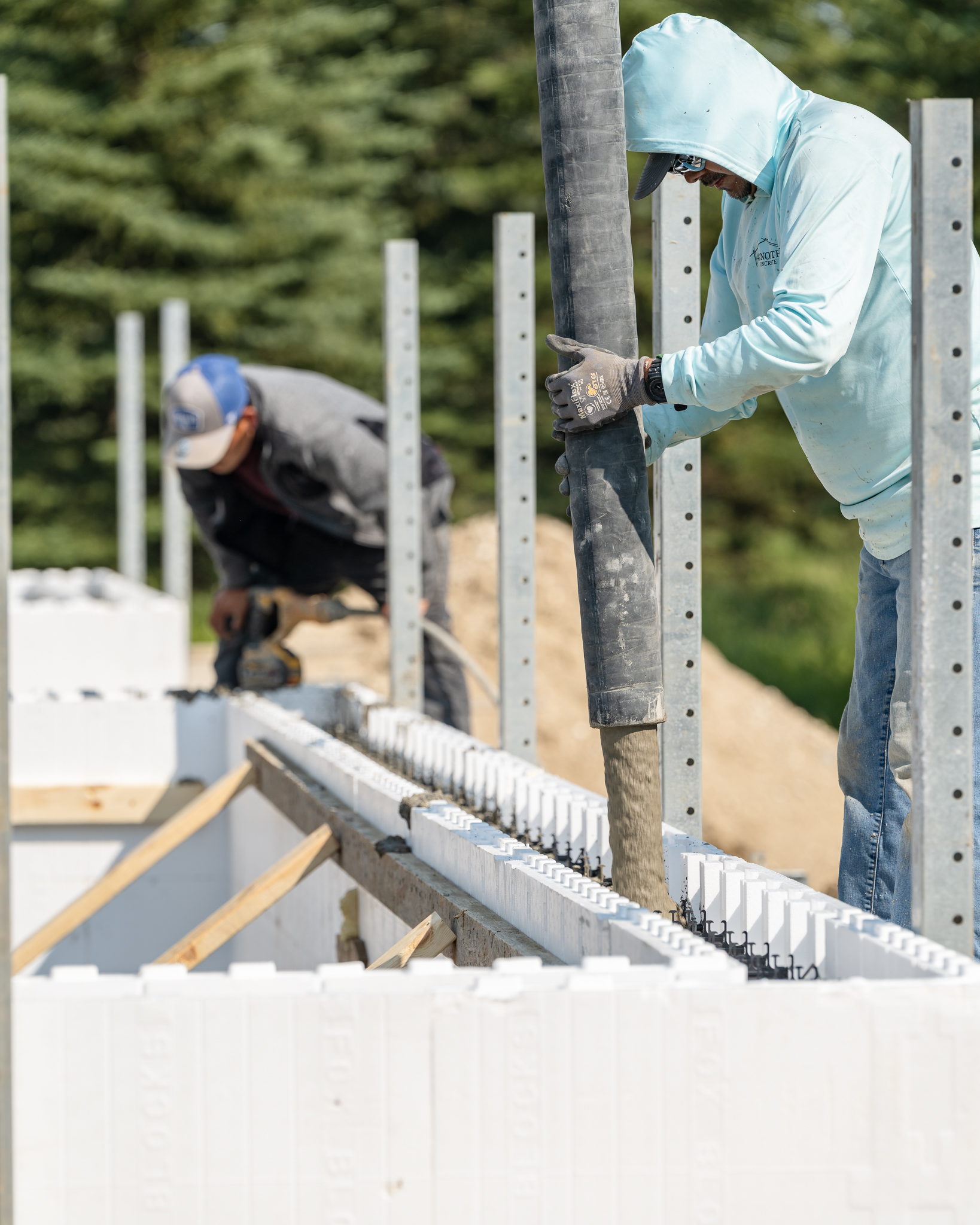 Two workers pouring concrete into ICF wall forms